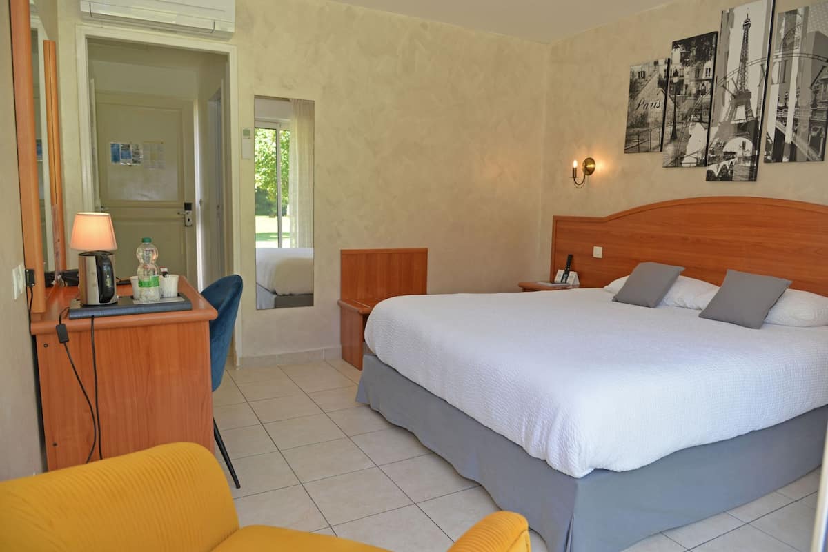 Ein Hotelzimmer mit einem Bett, einem Schreibtisch mit Lampe, einem Stuhl und Bildern an der Wand.
