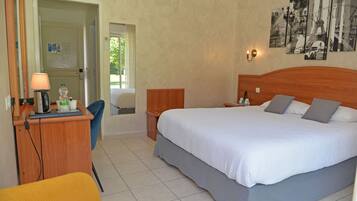 A hotel room with a bed, a desk with a lamp, a chair, and a wall with pictures.
