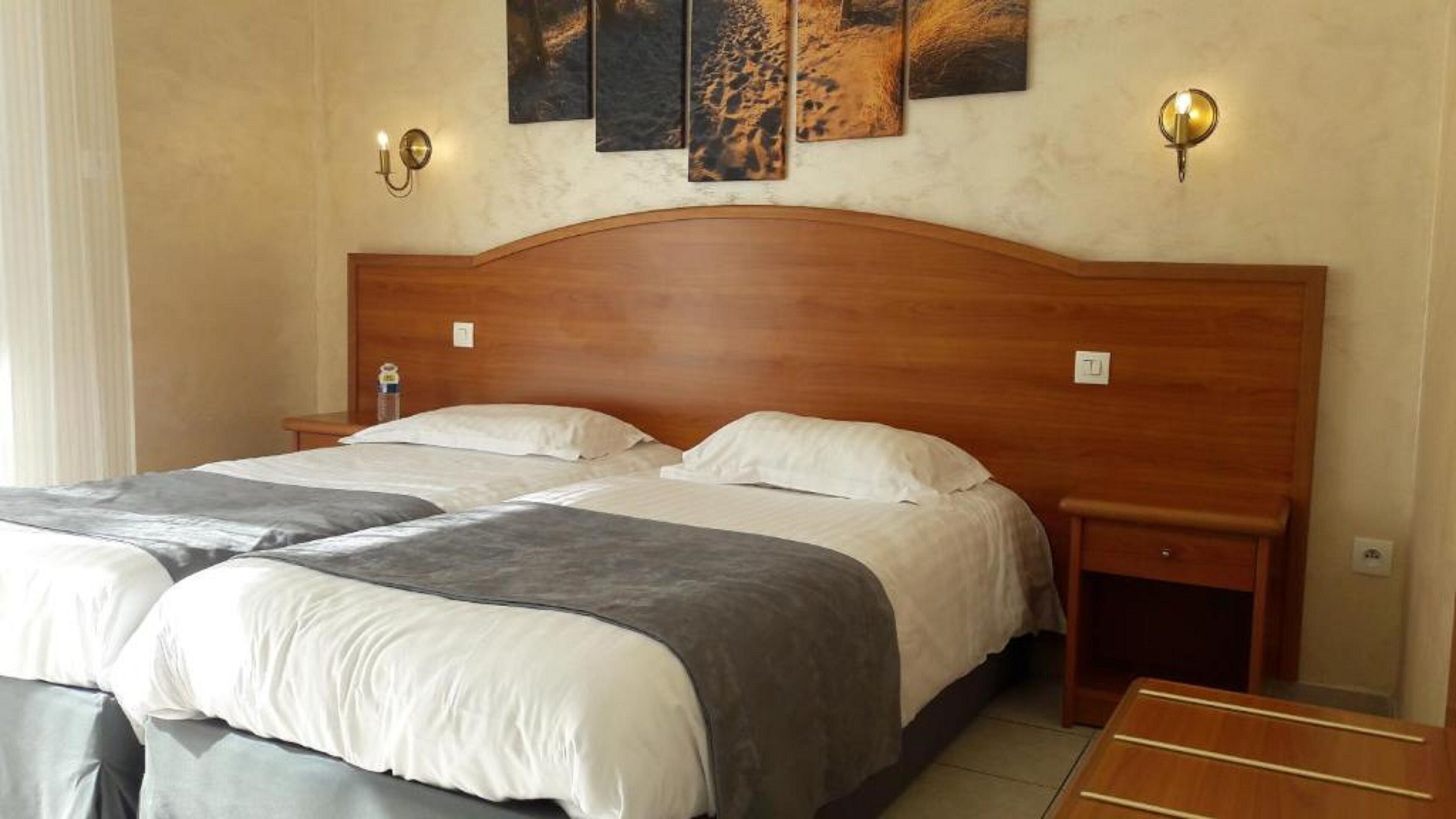 A double bed with two pillows and a blanket, wooden headboard, bedside tables, and wall-mounted light fixtures.