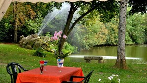 Un espacio de comedor al aire libre con una mesa lista para dos, rodeado de vegetación y una masa de agua.