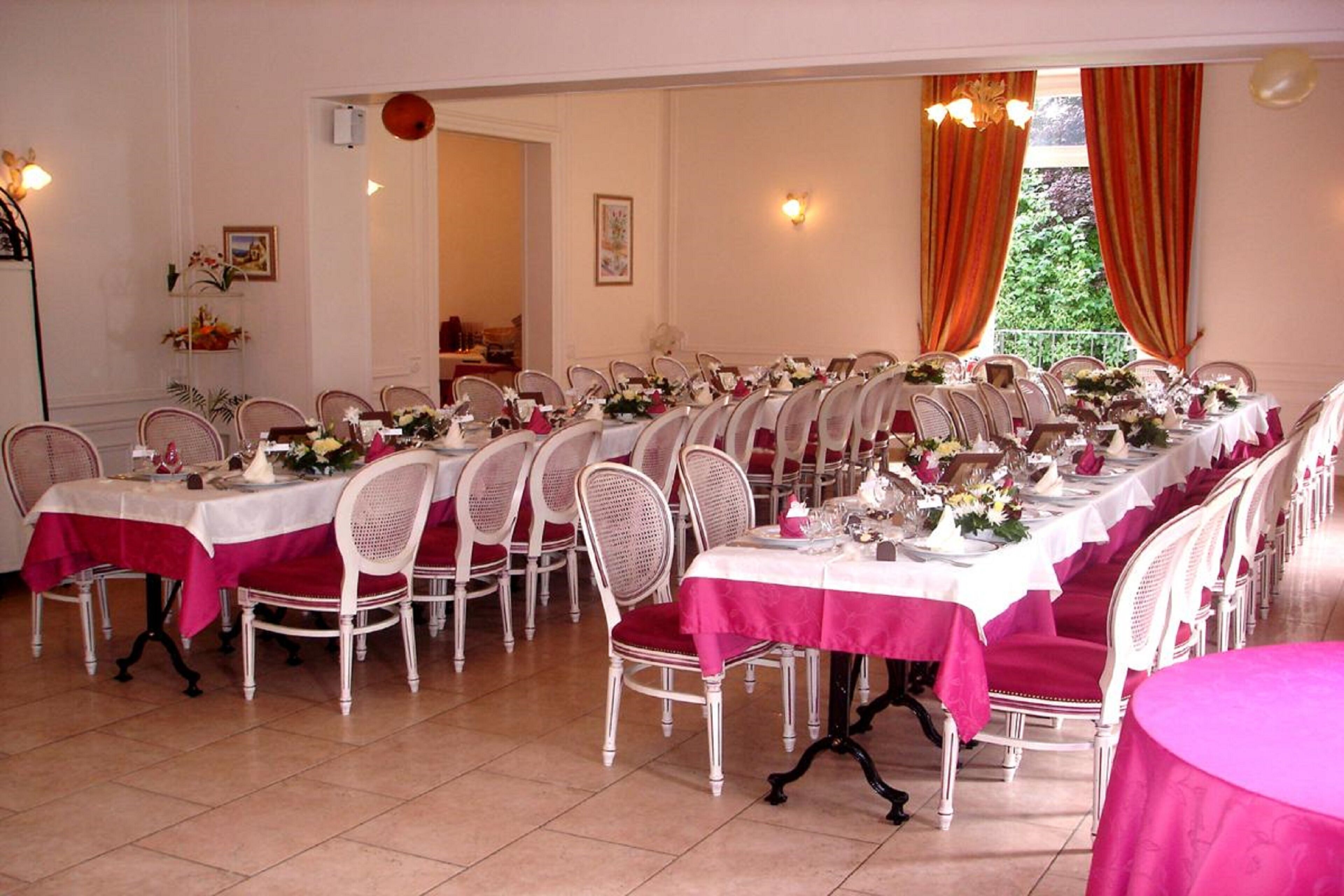 A dining area with multiple tables set for a meal, each with white chairs and red tablecloths.
