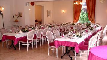 A dining area with multiple tables set for a meal, each with white chairs and red tablecloths.