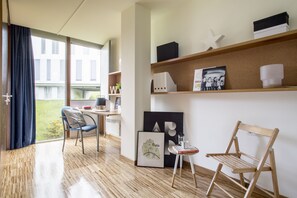 Una habitación moderna con suelo de madera, un escritorio con silla, una estantería y un ventanal con cortinas.