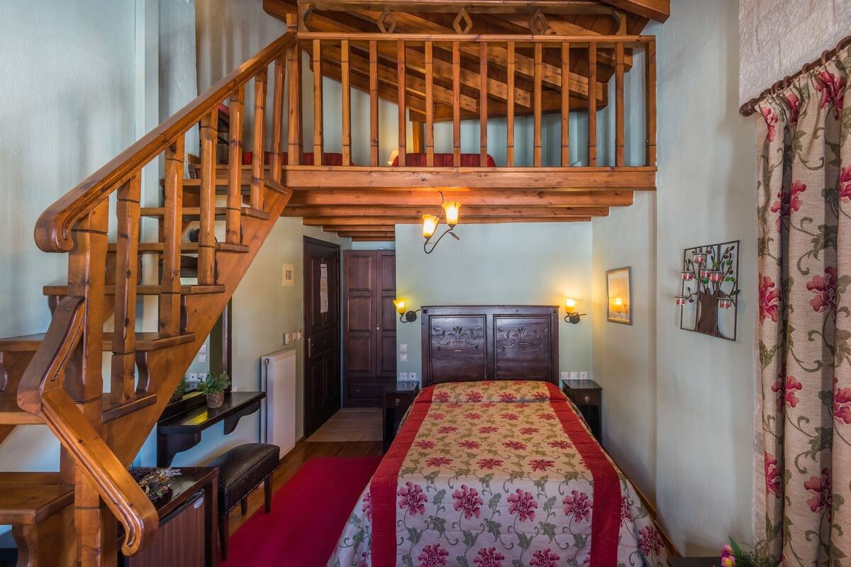 A bedroom with a wooden staircase, a bed with floral bedding, and a nightstand with a lamp.