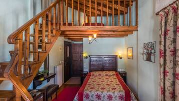 A bedroom with a wooden staircase, a bed with floral bedding, and a nightstand with a lamp.