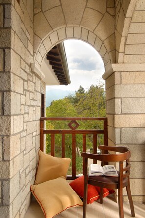 Un balcón de paredes de piedra con una silla de madera y cojines, con vistas a un paisaje verde exuberante.