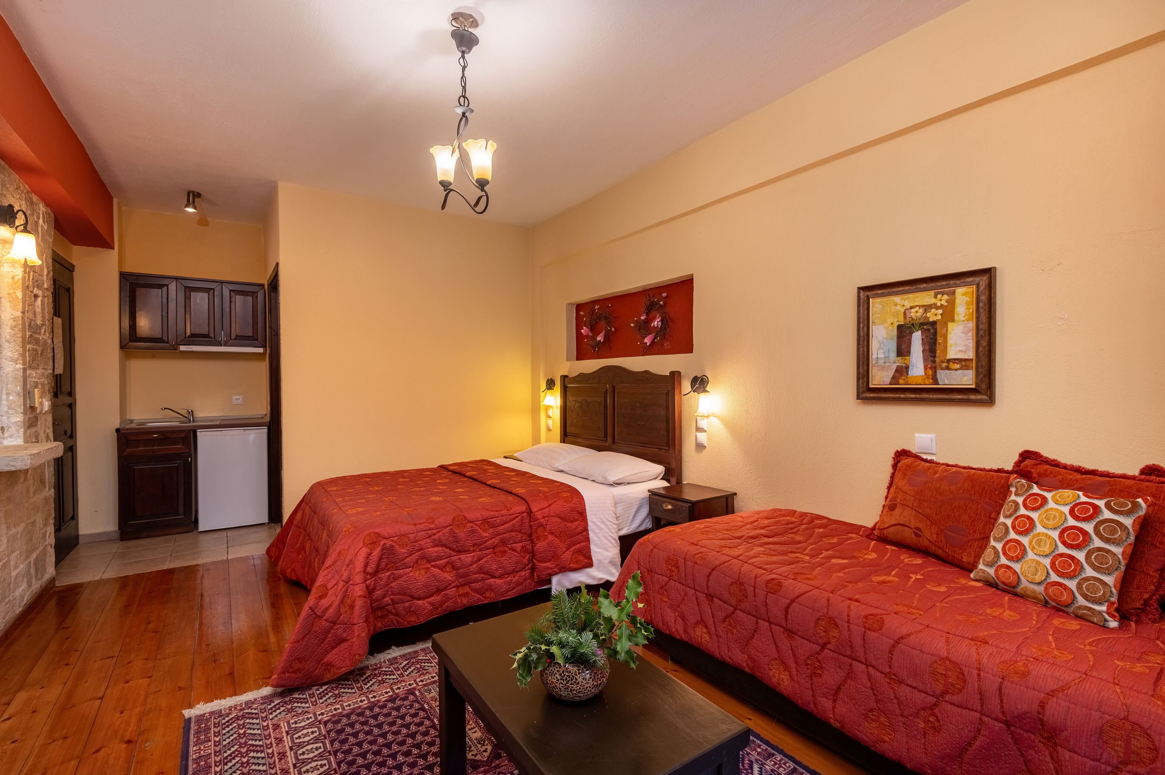 Una habitación de hotel con dos camas, una kitchenette pequeña, suelo de madera y una lámpara en el techo.
