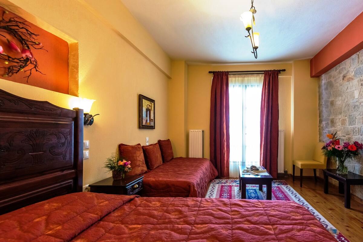 A hotel room with two beds, a wooden headboard, a small table with a vase, a chair, and a view of the outside.