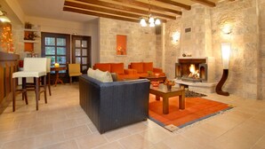 A cozy living room with a stone fireplace, wooden beams, and comfortable seating. - Mikri Arktos (Pyli)