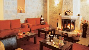 A cozy living room with a stone wall, a fireplace, a sofa, and a coffee table with candles and a bottle of wine. - Mikri Arktos (Pyli)
