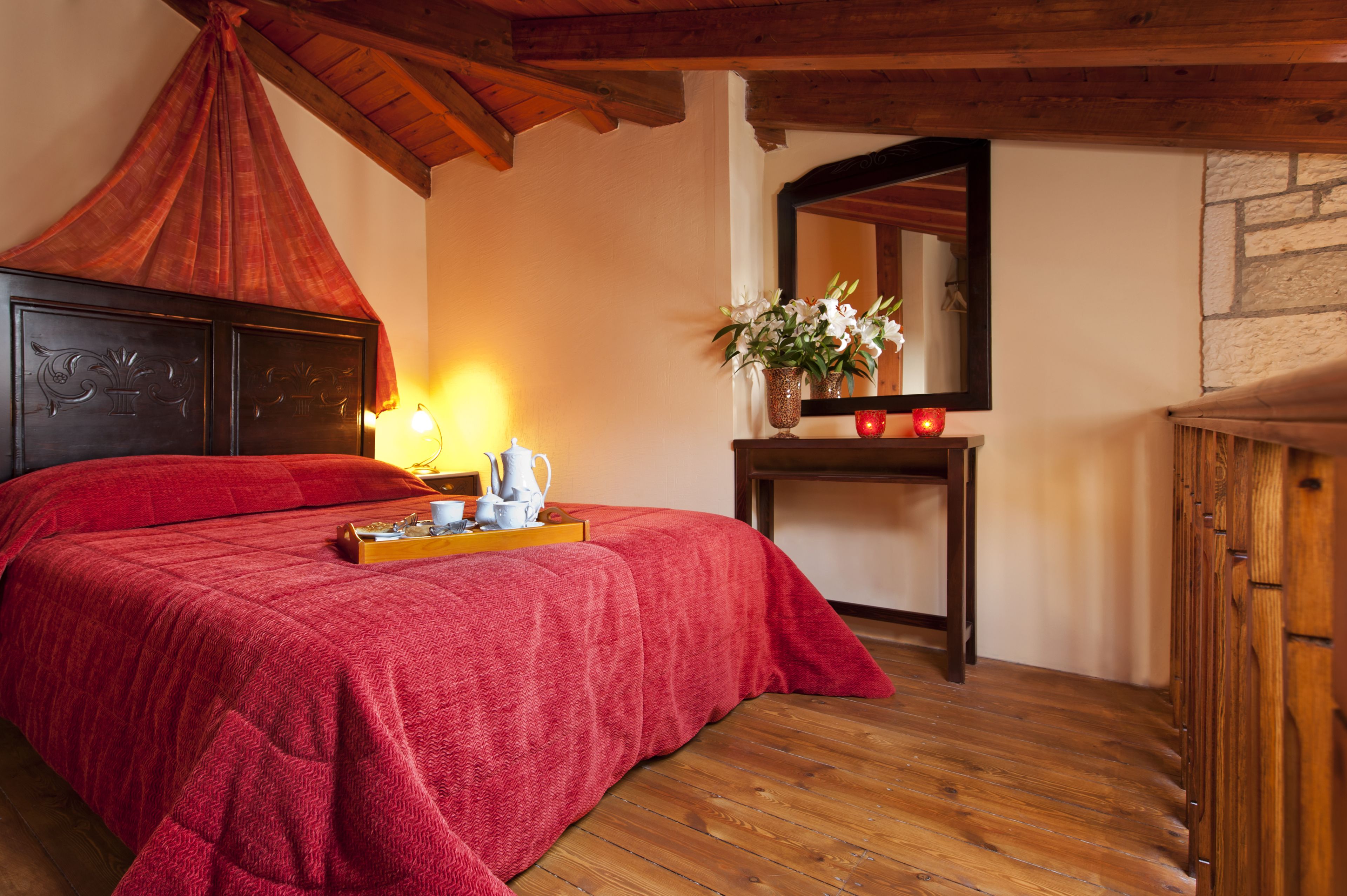 Una habitación con una cama, una mesita de noche con un jarrón de flores, un espejo y un armario de madera.