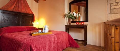 Una habitación con una cama, una mesita de noche con un jarrón de flores, un espejo y un armario de madera.