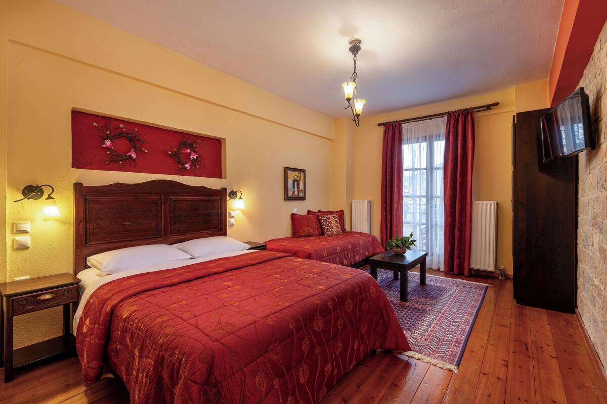 A hotel room with two beds, a wooden headboard, a red wall decoration, a small table, and a TV mounted on the wall.