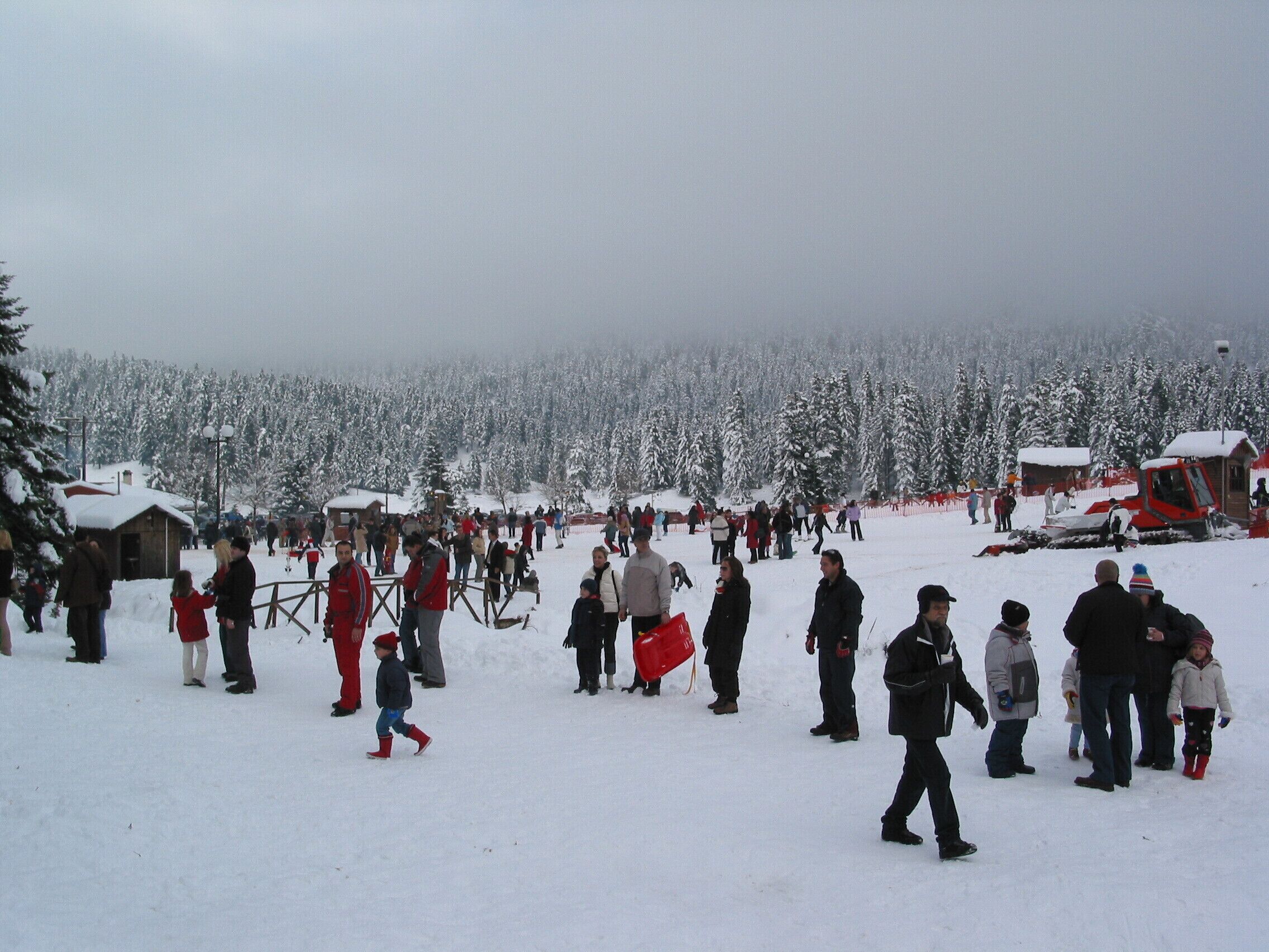 Uma área externa coberta de neve, com pessoas e um veículo vermelho.