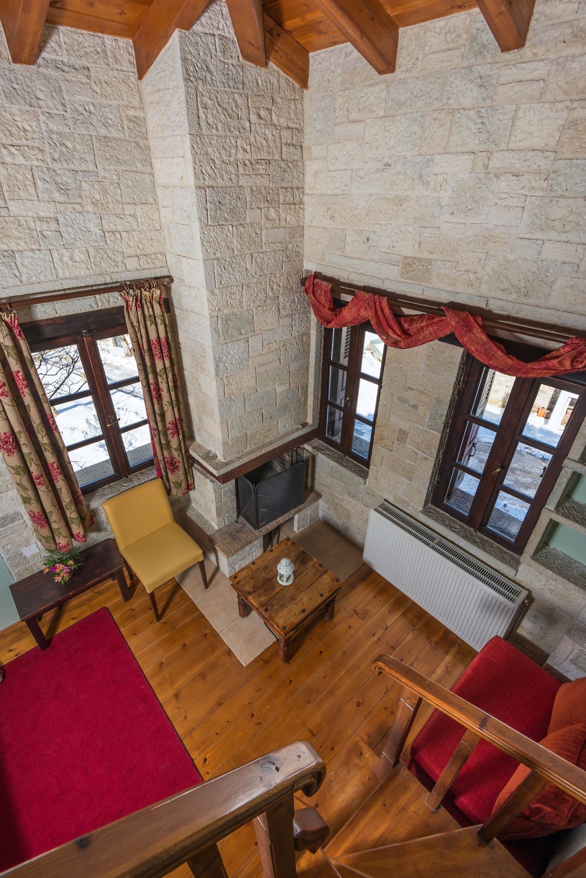 A cozy room with stone walls, a fireplace, wooden flooring, and a red carpet.