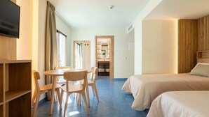 Habitación de hotel con televisión, mesa de comedor con sillas, cama y armario de madera.