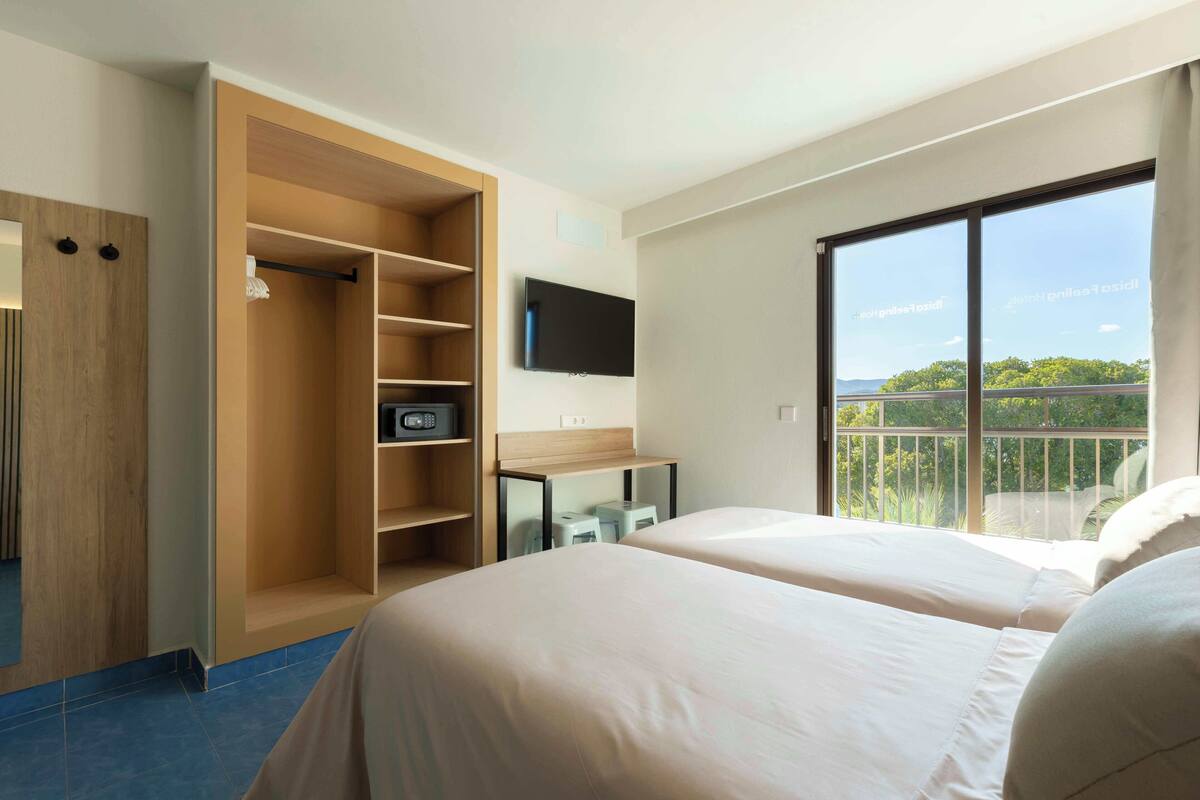 Ein Hotelzimmer mit zwei Betten, einem Fernseher, einem Kleiderschrank und einem Balkon mit Blick.