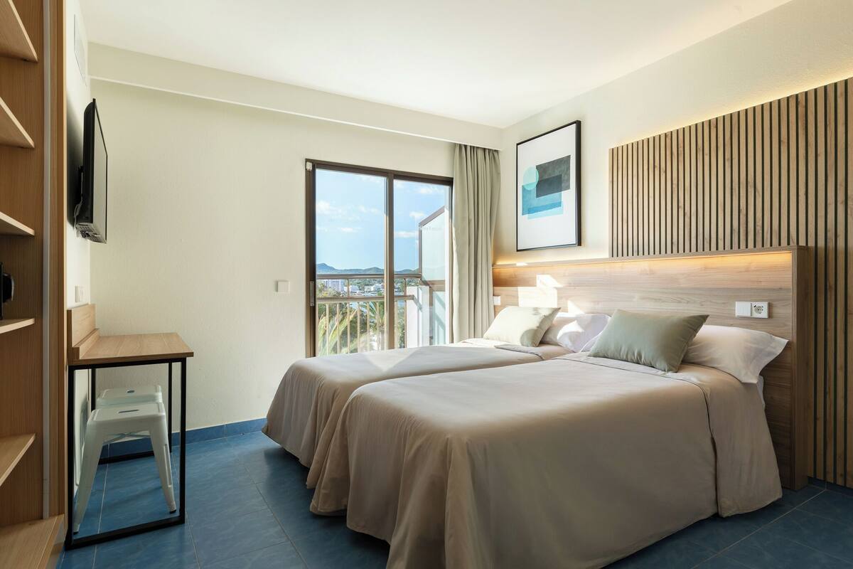 Ein Hotelzimmer mit zwei Betten, einem Schreibtisch, einem Fernseher und einem Balkon mit Blick.