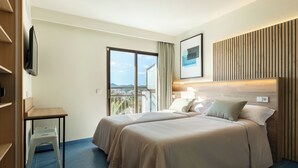 Habitación de hotel con dos camas, un escritorio, televisor y balcón con vistas.