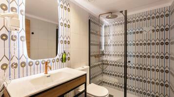 Un baño moderno con un lavabo blanco, un espejo, un inodoro y una zona de ducha con baldosas estampadas.