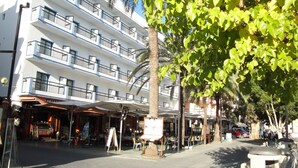 Un hotel de varios pisos con balcones, mobiliario exterior y una palmera.