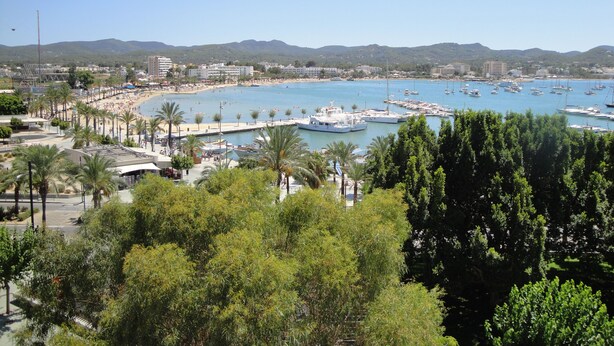Un pueblo costero con un puerto deportivo, playa y colinas circundantes.