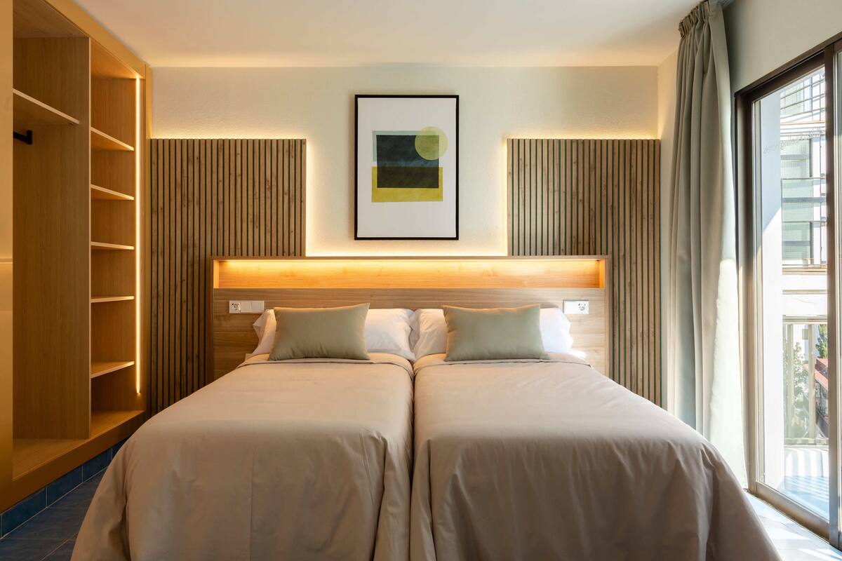Ein Hotelzimmer mit Doppelbett, einem Holzschrank, einem gerahmten Kunstwerk an der Wand und einem Fenster mit Vorhängen.