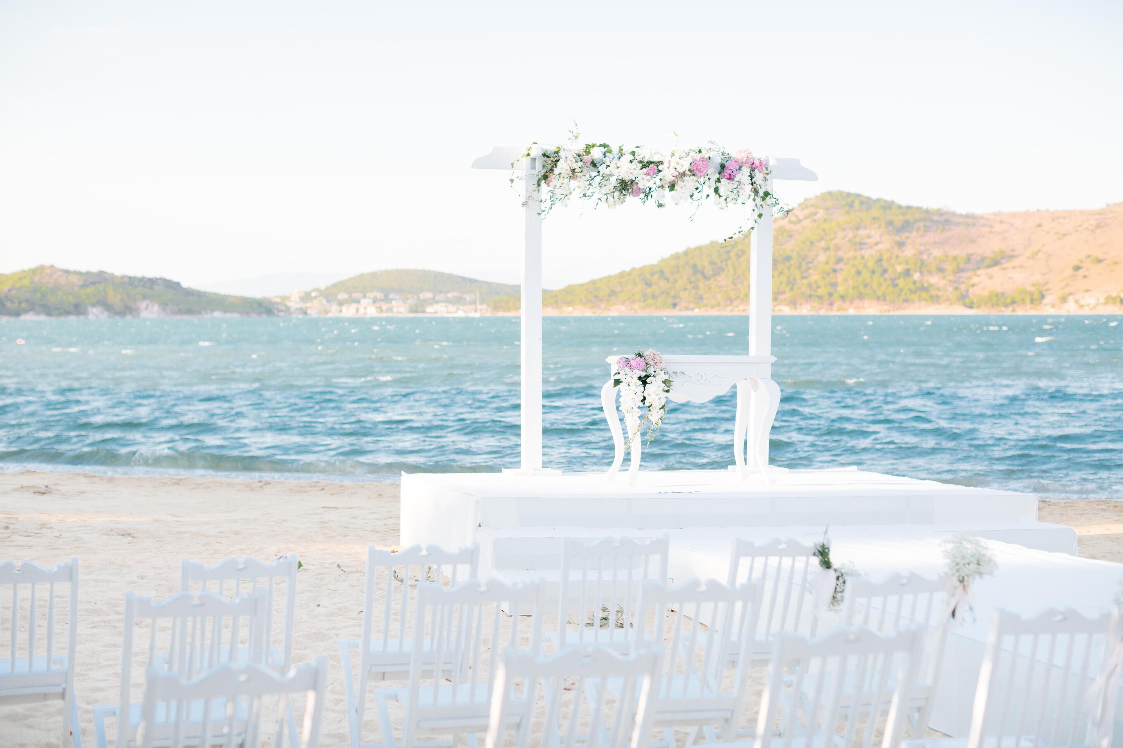 A beach wedding setup with a white arch and chairs.