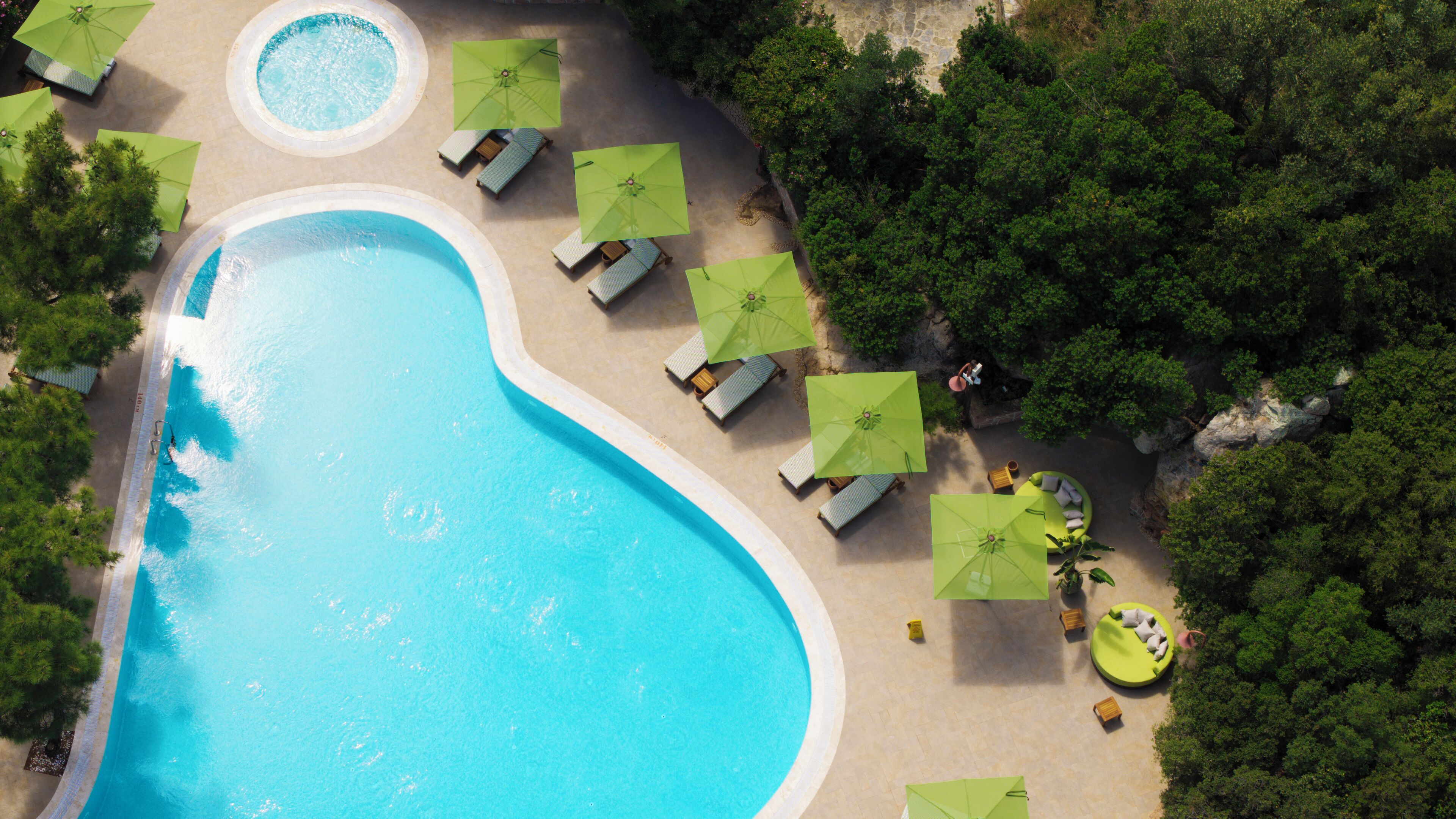 An aerial view of a swimming pool with lounge chairs and umbrellas, surrounded by dense greenery.