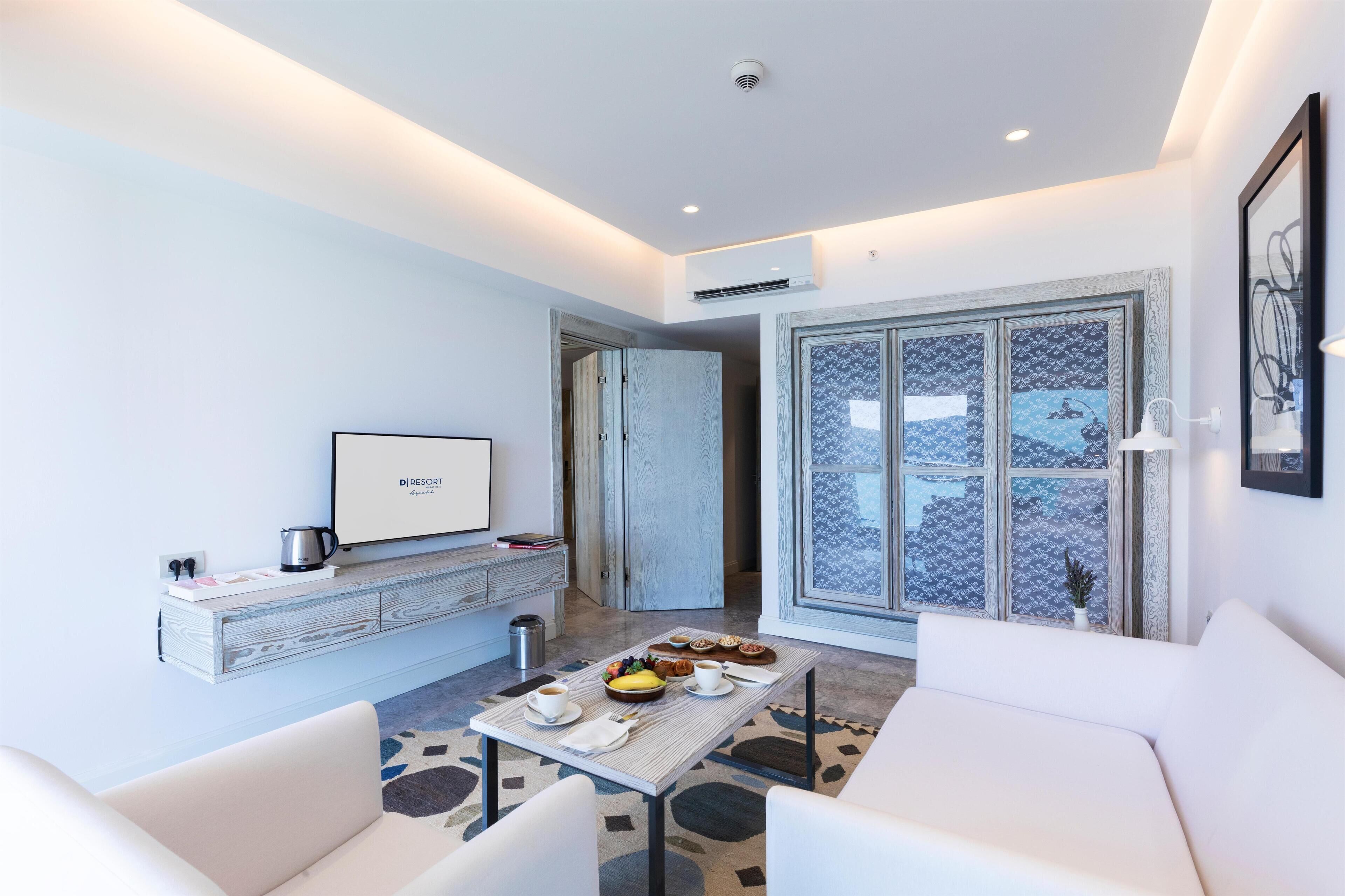 A modern living room with a flat-screen TV, a dining table with breakfast items, a sofa, and a large window with patterned curtains.