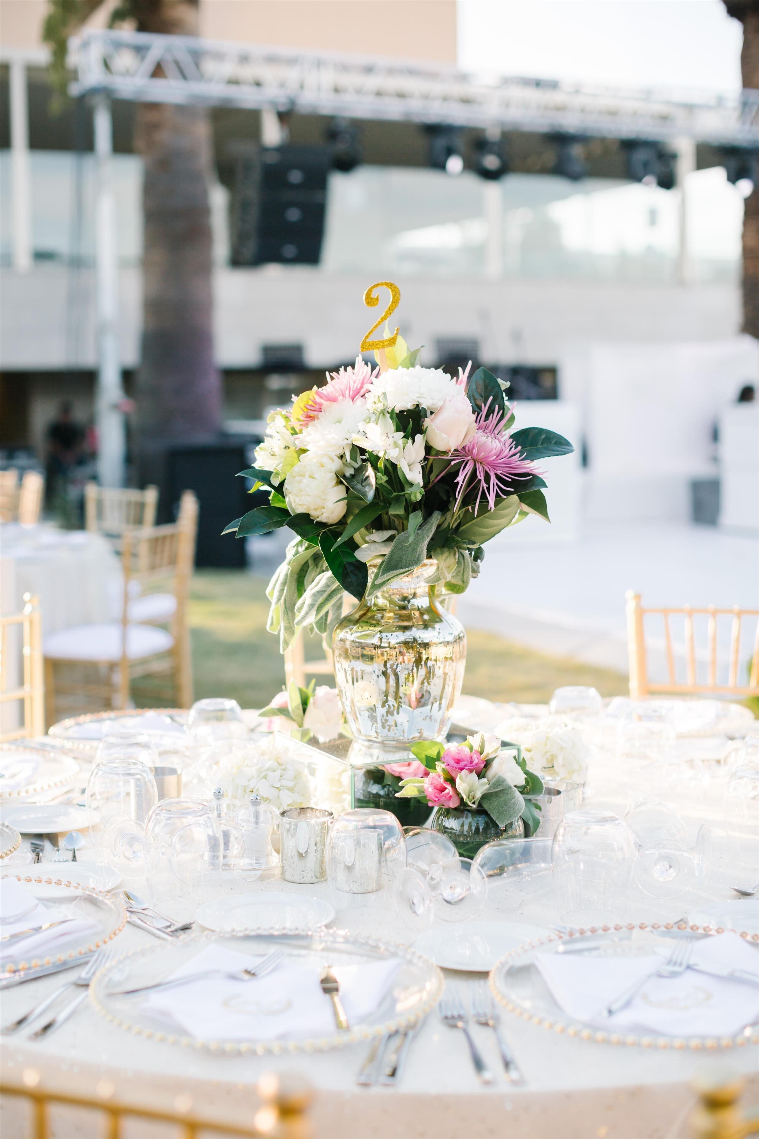 A table set for a wedding reception with a centerpiece of flowers and a number 2 topper.