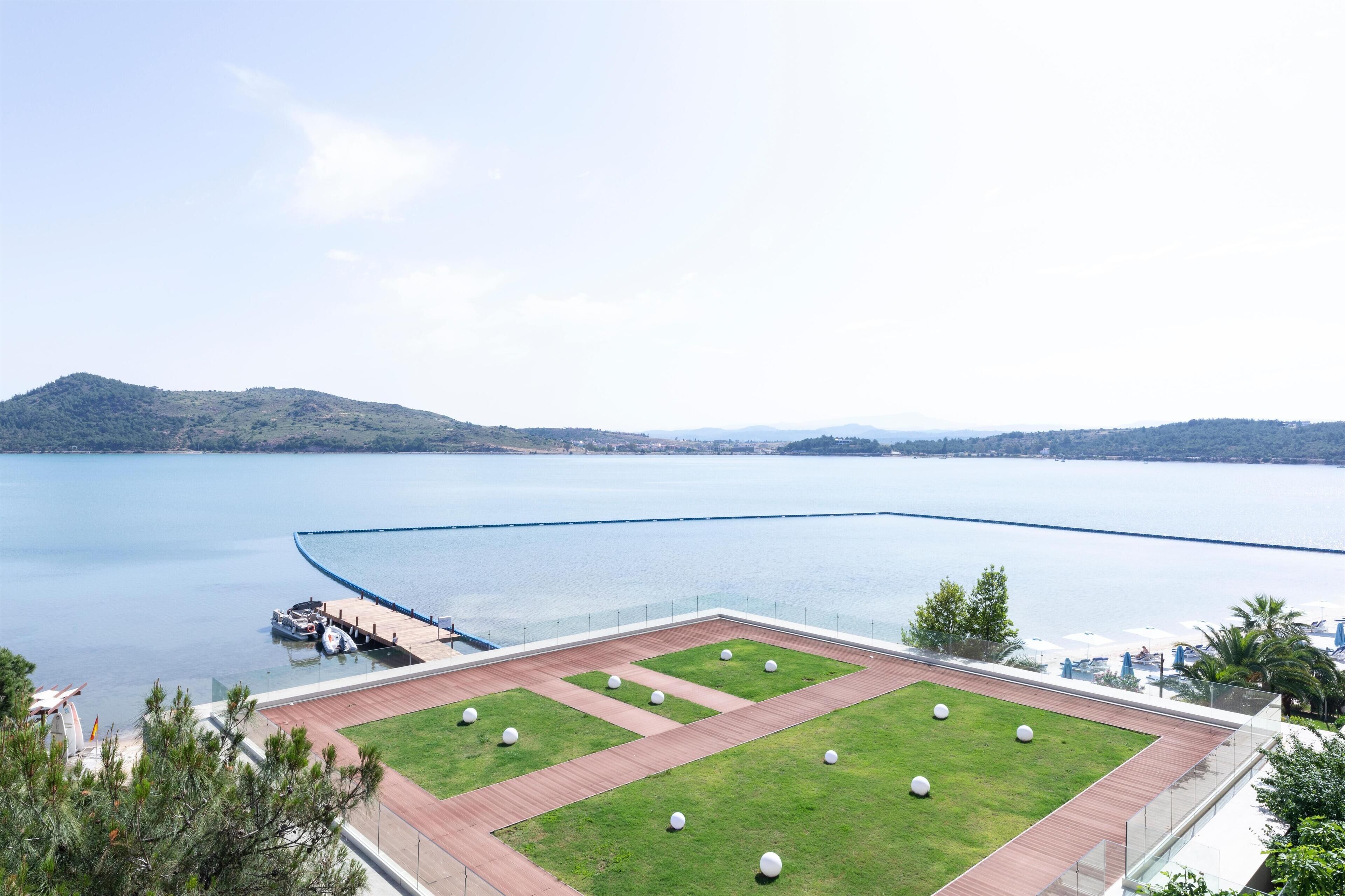 A waterfront hotel with a grassy deck, a pool, and a view of the lake and hills.