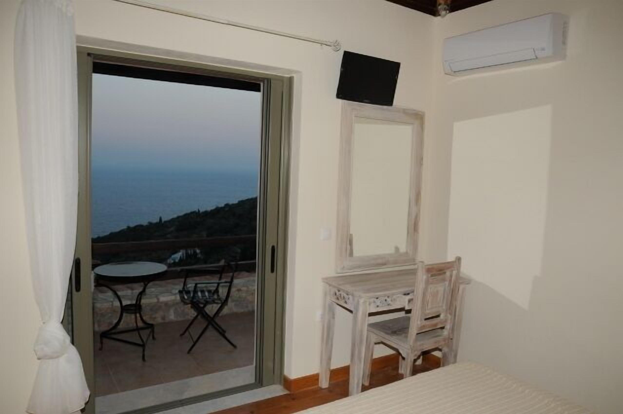 A room with a sliding glass door leading to an outdoor seating area with a table and chairs. There is a small wooden table and a chair inside the room.