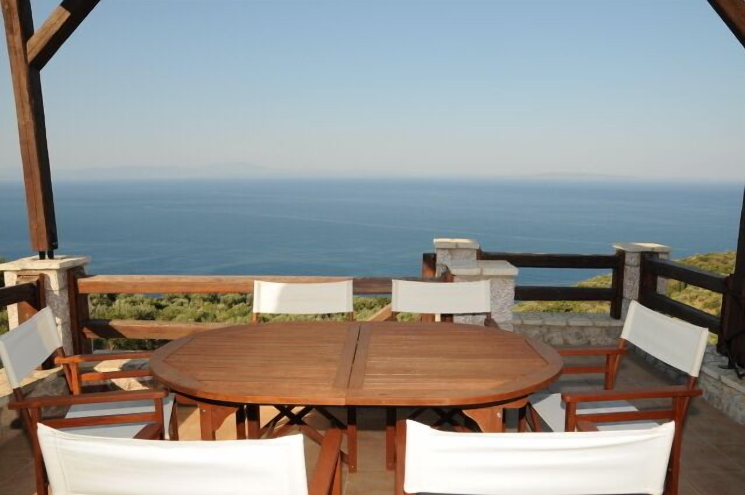Une table et des chaises en bois sont disposées sur une terrasse offrant une vue sur la mer.