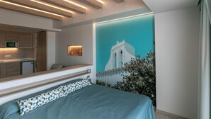 A modern bedroom with a bed, a built-in bench, a wall-mounted TV, and a kitchen area in the background. - The White Apartments by Ibiza Feeling - Adults Only (Sant Antoni de Portmany)