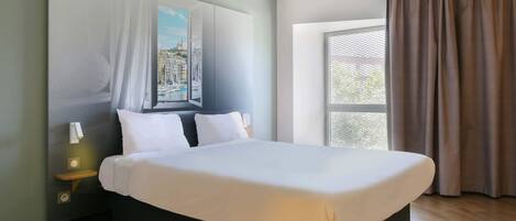 Un dormitorio moderno con una cama grande, una mesita de noche, una lámpara de pared y una ventana con cortinas.