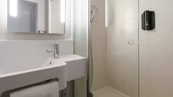 Un baño moderno con un lavamanos blanco, un espejo y una zona de ducha con mampara de vidrio.