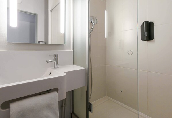 A modern bathroom with a white sink, a mirror, and a glass-enclosed shower area.