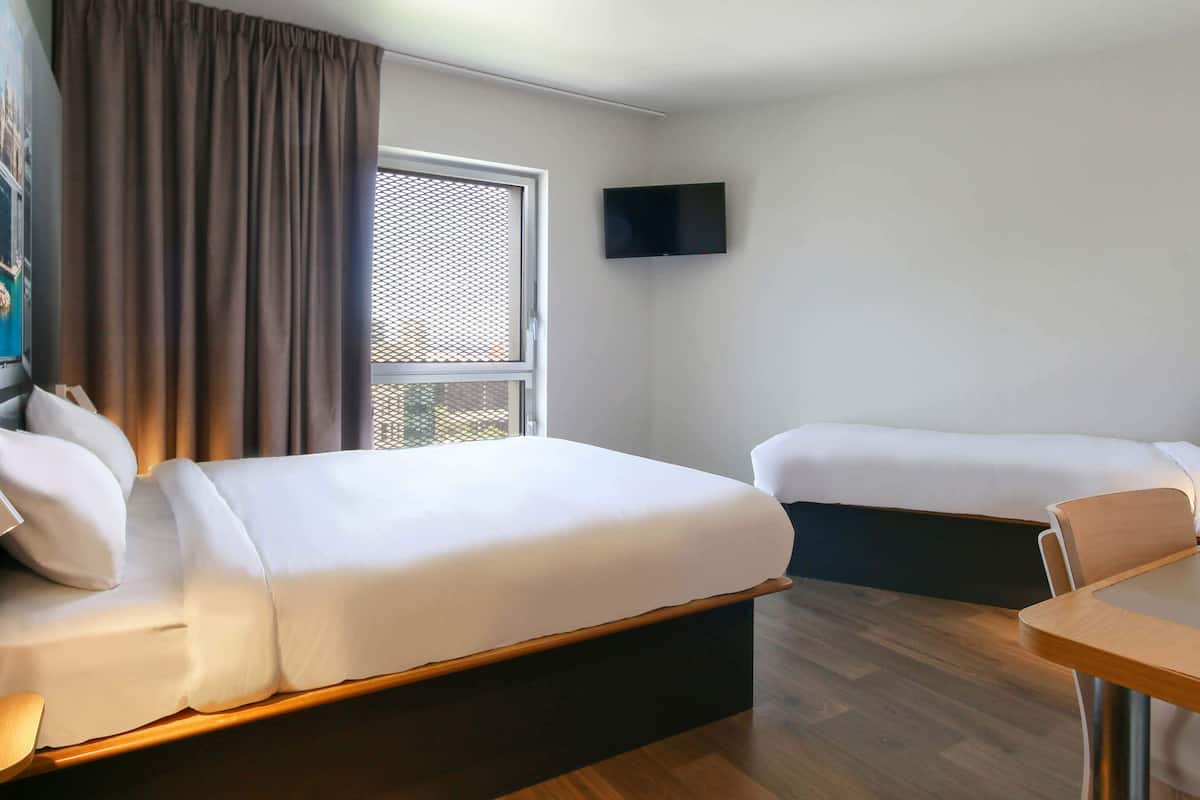 A hotel room with two beds, a TV, a window with curtains, and a wooden table.
