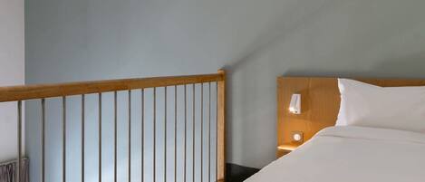 A hotel room with a wooden headboard, a bedside table with a lamp, and a view of a balcony with a railing.