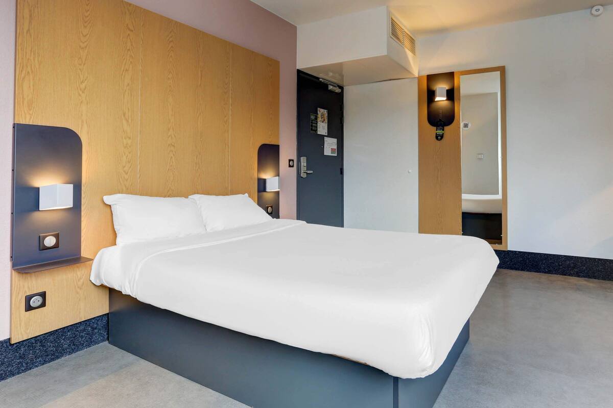 Ein modernes Hotelzimmer mit einem großen Bett, Holzvertäfelung und integrierter Beleuchtung.