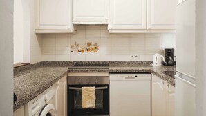 A compact kitchen with white cabinetry, a granite countertop, a washing machine, an oven, and a dishwasher. - Apartamentos Ona Club Bena Vista (Estepona)