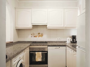 A compact kitchen with white cabinetry, a granite countertop, a washing machine, an oven, and a dishwasher. - Apartamentos Ona Club Bena Vista (Estepona)
