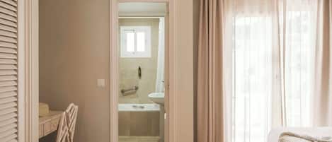 Habitación de hotel con cama, escritorio y baño visible a través de una puerta abierta.