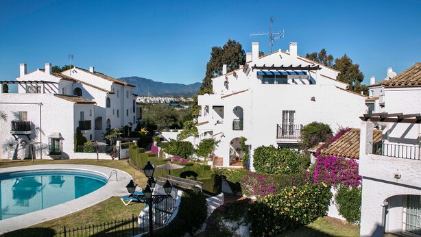 A white villa with a swimming pool, surrounded by lush gardens and a clear view of the mountains. - Apartamentos Ona Club Bena Vista (Estepona)