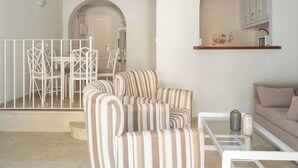 A living room with striped armchairs, a glass coffee table, a sofa, and a kitchen area with cabinets and a tiled backsplash. - Apartamentos Ona Club Bena Vista (Estepona)