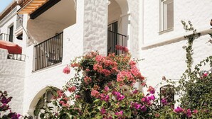 Un edificio blanco con tejado de tejas, ventanas arqueadas y balcones con barandillas de metal.