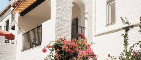 Un edificio blanco con tejado de tejas, ventanas arqueadas y balcones con barandillas de metal.