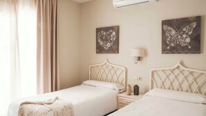 A hotel room with two beds, a nightstand, a lamp, and two wall-mounted floral artwork. - Apartamentos Ona Club Bena Vista (Estepona)