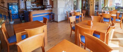A restaurant with wooden tables and chairs, a bar area, and a stone wall.
